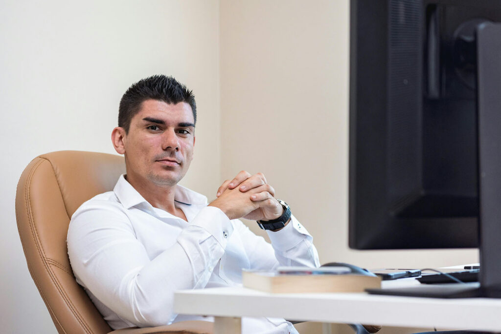 Man in White Long Sleeves Sitting on Brown Chair with his Hands Together
